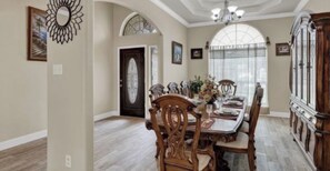 Uma sala de jantar com uma mesa e cadeiras de madeira, um lustre e um armário grande de madeira com portas de vidro.