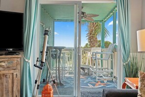 Une chambre dotée d’une télévision, d’un télescope et d’un balcon avec des chaises et un palmier.