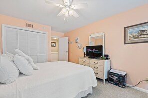 A bedroom with a bed, a television, a dresser, a mirror, and a ceiling fan. - Oceanfront 2 BR Villa-Pool-Corner Balcony-King Bd (North Myrtle Beach)