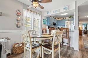 A dining area with a round table and chairs, a ceiling fan, and a kitchen in the background. - Oceanfront 2 BR Villa-Pool-Corner Balcony-King Bd (North Myrtle Beach)