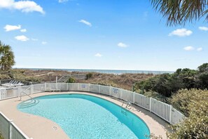 A curved pool with a white fence, surrounded by vegetation and a view of the beach. - Oceanfront 2 BR Villa-Pool-Corner Balcony-King Bd (North Myrtle Beach)