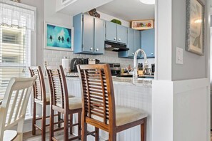 A kitchen with a central island, bar stools, and a dining table with chairs. - Oceanfront 2 BR Villa-Pool-Corner Balcony-King Bd (North Myrtle Beach)