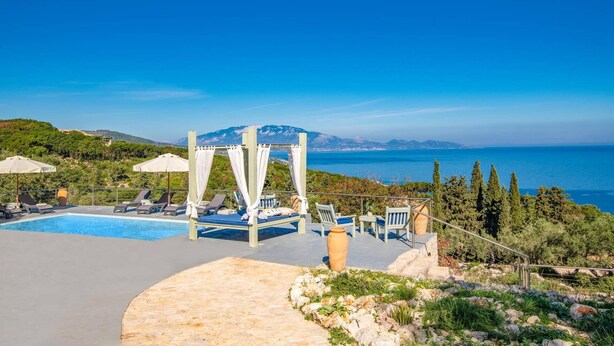 A poolside area with lounge chairs, a pergola, and a view of the sea and mountains. - Villa Thea by Villa Plus (Ionian Islands)