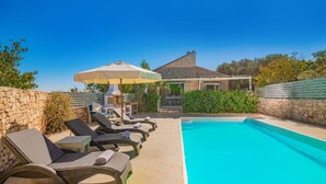 A pool area with lounge chairs and a pergola with an umbrella.