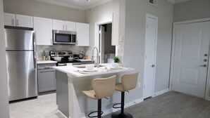 A modern kitchen with white cabinets, stainless steel appliances, and a central island with two bar stools. - Cozy 1BR Magnolia Pool, Gym & Free Parking (Magnolia)