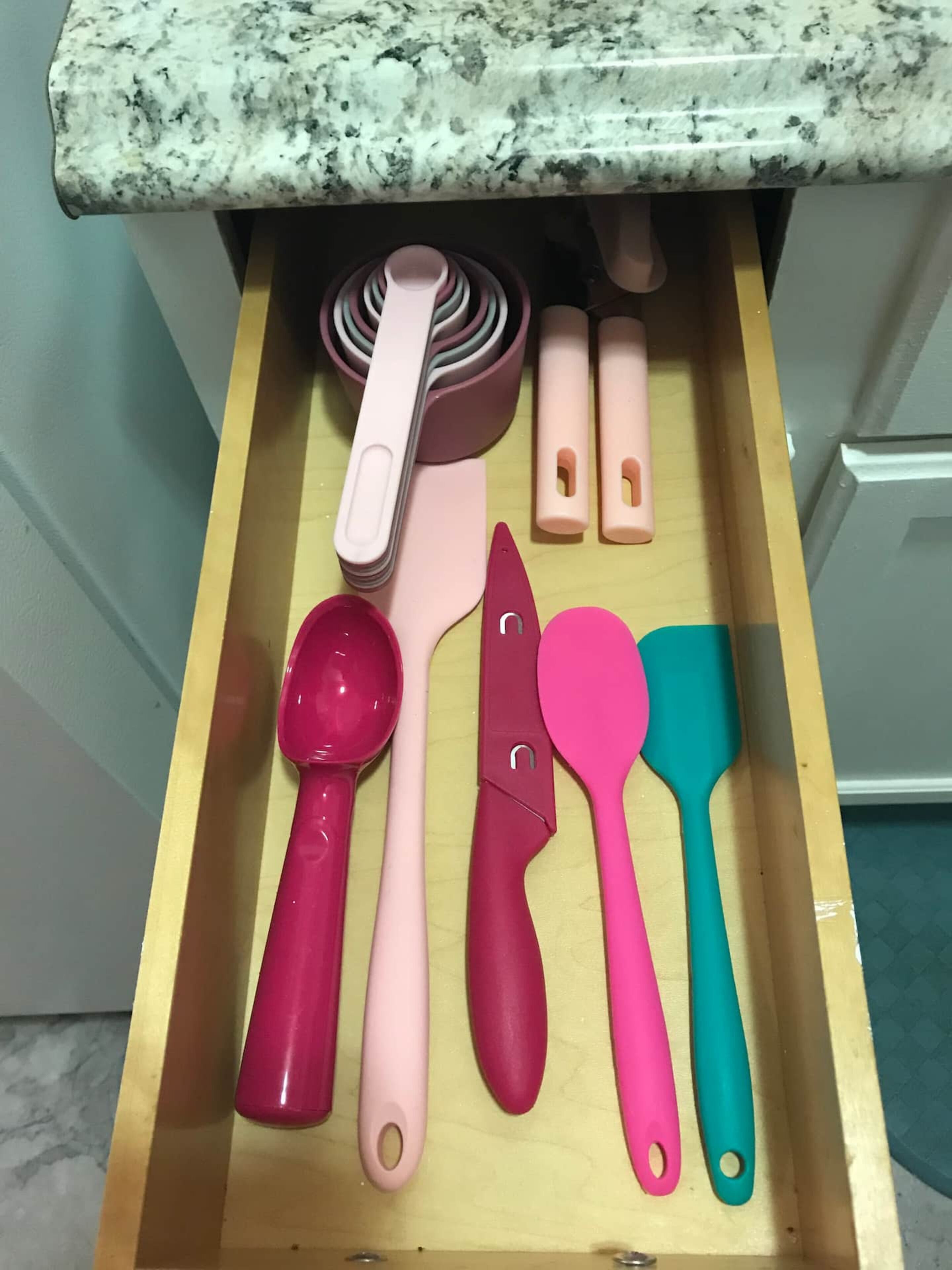 A drawer containing kitchen utensils with handles in various colors.