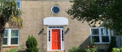 A two-story brick building with a red door, a small porch, and a mailbox.