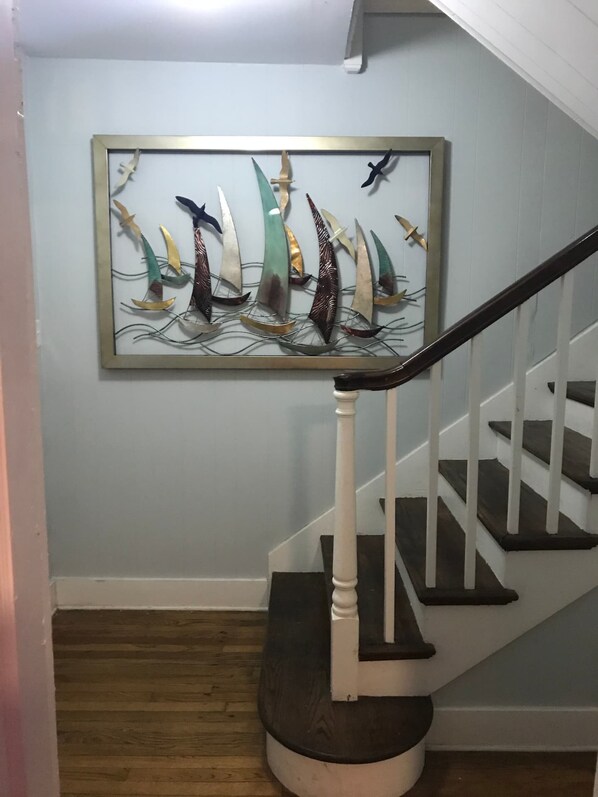 Eine Treppe mit weißen Balustraden und dunklen Stufen, die zu einer Zwischenebene führt, wo ein gerahmtes Kunstwerk mit Segelbooten an der Wand hängt.