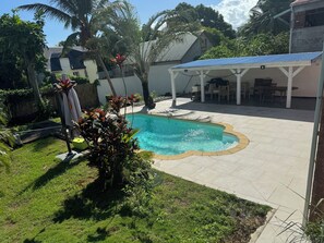 A backyard with a swimming pool, a covered patio area, and surrounding greenery. - Studio pool in the center of the gullet (Le Gosier)