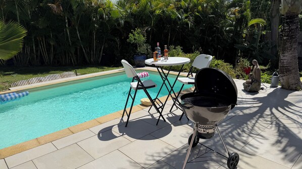 A poolside area with a barbecue grill, chairs, and a table. - Studio pool in the center of the gullet (Le Gosier)