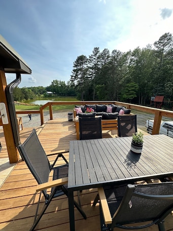 A wooden deck with a table and chairs, overlooking a lake and forest.