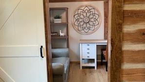 A cozy room with a wooden ceiling, a chandelier, a desk with drawers, a chair, and a decorative wall piece. - Log Cabin at the Farm (Siler City)