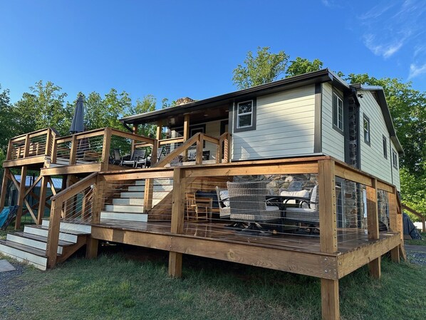 Une maison en bois à deux étages, dotée d’une terrasse, d’un espace salon extérieur et d’une cheminée en pierre.