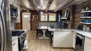A kitchen with a central island, wooden flooring, and a stone accent wall. - Log Cabin at the Farm (Siler City)