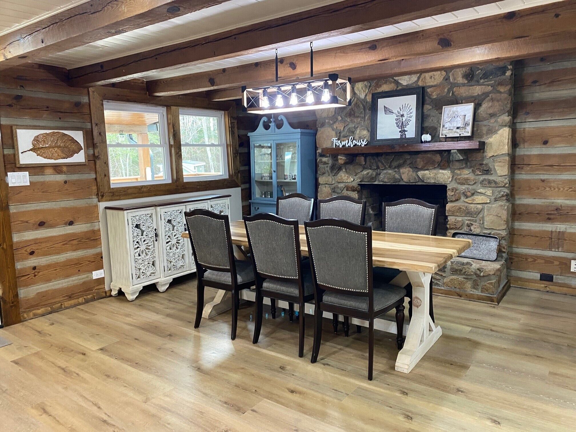 Un coin repas rustique avec une table et des chaises en bois, une cheminée en pierre et une fenêtre donnant sur la forêt.