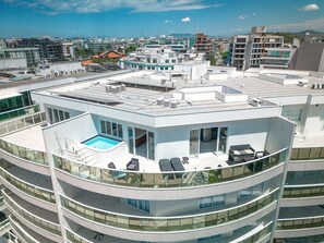 Een modern gebouw met een zwembad op het dak, meerdere balkons en uitzicht op de stadsgezicht.