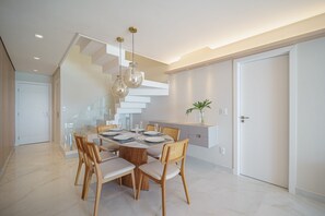 Een moderne eethoek met een tafel met glazen blad, houten stoelen en een hanglamp.