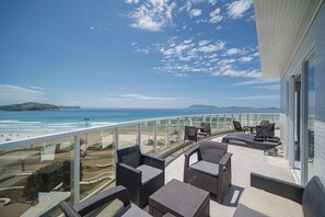 Ein Balkon mit Korbmöbeln mit Blick auf einen Strand und den Ozean.