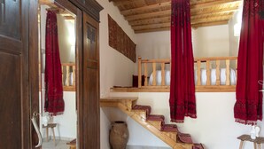 Un escalier en bois, des rideaux rouges, une porte en bois et un vase blanc posé sur le sol.