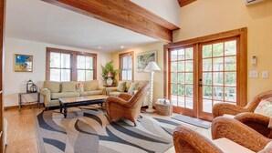 A spacious living room with a high ceiling, wooden beams, a beige sofa, wicker chairs, a coffee table, and large windows with blinds. - Passover Cottage | Private Pool & Ideal Key West Location (Key West)