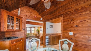 A wooden interior with a glass dining table and chairs, wooden cabinets, and a ceiling fan. - Passover Cottage | Private Pool & Ideal Key West Location (Key West)