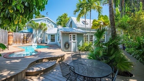 A backyard with a swimming pool, a hot tub, and a wooden deck with a metal table and chairs. - Passover Cottage | Private Pool & Ideal Key West Location (Key West)