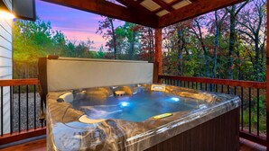 Ein Whirlpool auf einer Holzterrasse mit Blick auf Bäume und einen Sonnenuntergang.