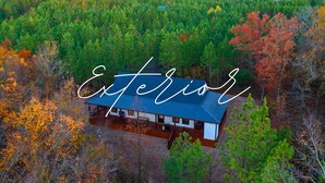Luftaufnahme einer Hütte, umgeben von dichtem Wald, mit blauem Himmel.
