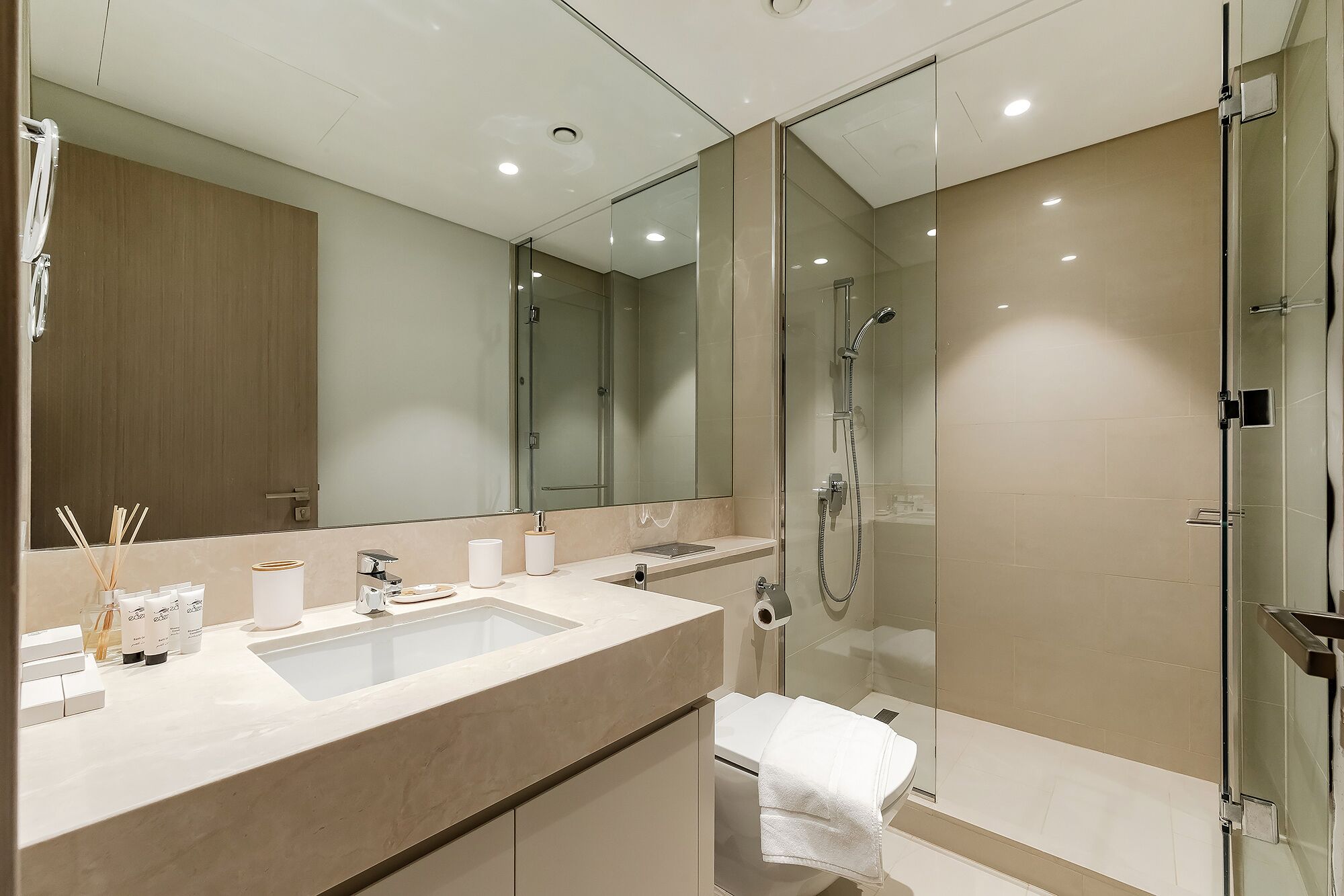 A modern bathroom with a large mirror, a glass-enclosed shower, and a beige vanity with a sink and towel rack.