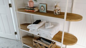 A wooden shelf unit with folded towels, a vase with shells, and books.