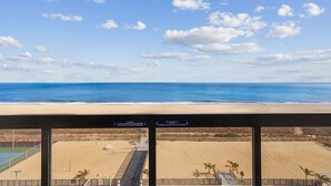 Une vue sur la plage depuis un balcon, avec un court de tennis et un panneau indiquant l’absence de garde-corps.