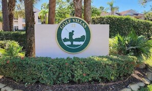 Señal para Golf Villas, con silueta de golfista, rodeada de follaje y palmeras.