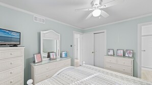 Une chambre à coucher comprenant un lit, une commode, un miroir et un ventilateur de plafond.
