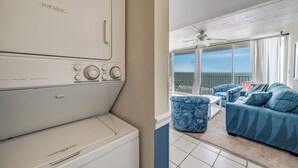 Une buanderie équipée d’un grand lave-linge et d’un grand sèche-linge, un balcon avec vue et un canapé bleu à motifs.