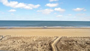 Une plage avec un rivage sablonneux et une clôture en bois au premier plan.