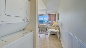 A hotel room with a washing machine, a small table, a chair, and a view of the sea through large windows. - Sea Gate 307 by Seaside Vacations & Sales (Ocean City)