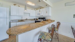 A kitchen with white cabinets, a granite countertop, a built-in microwave, and a coffee maker. There are two chairs with woven seats and metal frames. - Sea Gate 307 by Seaside Vacations & Sales (Ocean City)