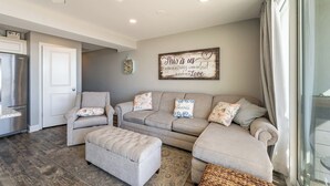 A living room with a gray sofa set, a small ottoman, and a decorative wall piece.