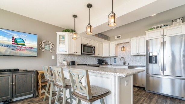 A modern kitchen with white cabinets, stainless steel appliances, and a bar area with wooden stools.