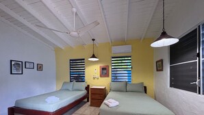 Una habitación con dos camas, un aparador de madera, un ventilador de techo y una ventana con persianas.