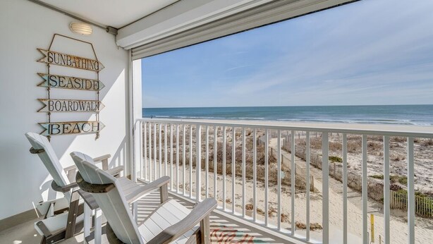 Un balcon avec vue sur la plage, agrémenté d’un panneau indiquant le chemin vers l’endroit où se baigner au soleil, vers le bord de mer, la promenade et la plage.