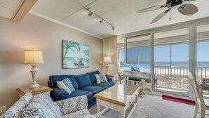 A hotel room with a balcony, a sofa, a coffee table, and a painting of a beach scene. - Sea Gate 205 by Seaside Vacations & Sales (Ocean City)