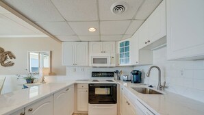 A compact kitchen with white cabinetry, a built-in microwave, an oven, a sink, and a coffee maker. - Sea Gate 205 by Seaside Vacations & Sales (Ocean City)