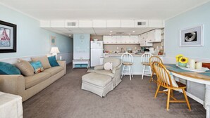 A compact living space with a kitchenette, a dining area with a table and chairs, and a sofa with cushions. - Stunning condo steps from the beach by Seaside Vacations & Sales (Ocean City)