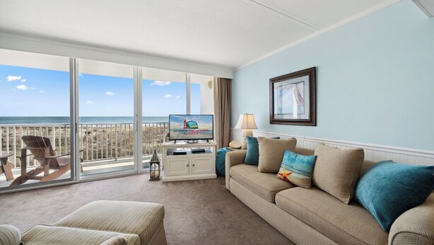 A hotel room with a balcony, a sofa, a TV, and a framed picture on the wall. - Stunning condo steps from the beach by Seaside Vacations & Sales (Ocean City)
