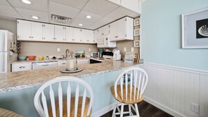A kitchen with white cabinets, a granite countertop, and two white bar stools. - Stunning condo steps from the beach by Seaside Vacations & Sales (Ocean City)