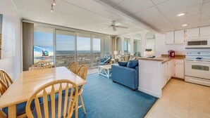 Amplia sala de estar con balcón vistas al mar, una mesa de comedor, un sofá y una zona de cocina.