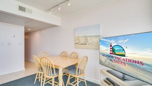 Una habitación moderna con una mesa de comedor, sillas, un televisor de pantalla plana y un cuadro con una playa.