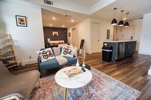 A modern living room with a sofa, coffee table, and a kitchen area with a sink and cabinets.