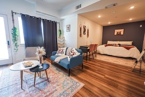 A modern hotel room with a bed, a sofa, a desk, and a small table.